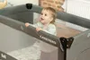 A baby is standing in a travel crib. Anteprima dell’immagine prodotto