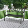 A black metal garden bench with an ornate backrest featuring birds and branches, placed on a grey wooden deck with a white railing and a green lawn in the background. Produktbild-Vorschau