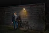 A man stands next to a bicycle in front of a wooden wall with a light fixture. Produktbild-Vorschau