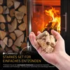 A hand holding fire starters in front of a fireplace with a stack of firewood in the background. Produktbild-Vorschau