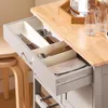 A close-up view of an open kitchen drawer with cutlery and a cloth inside, on a kitchen cart. Voir les images du produit