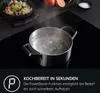 A pot of boiling water on a black induction cooktop, with a salad and fruit in the background. Podgląd zdjęcia produktu
