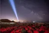 A person shines a flashlight into the night sky on a rocky shore. Podgląd zdjęcia produktu