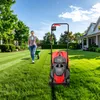 A woman is pushing a wheelbarrow on a lawn with a lawnmower in the foreground. Produktbild-Vorschau