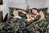 A mother and her two young children are lying in bed, snuggled under a black and gold floral duvet cover. Podgląd zdjęcia produktu