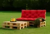 Outdoor furniture set made of wooden pallets with red cushions and a green throw blanket, placed on a grassy lawn. Produktbild-Vorschau