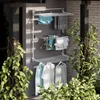 A wall-mounted drying rack with clothes hanging on it, situated on a balcony or patio with plants in the foreground. Produktbild-Vorschau