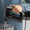 A person is holding a black Bosch hand mixer over a glass bowl. Produktbild-Vorschau