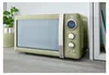 A retro-style green microwave oven is placed on a wooden countertop next to a plant and a shelf with books. Voir les images du produit