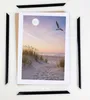 A framed picture of a beach scene with a seagull flying overhead, surrounded by frame pieces. Produktbild-Vorschau