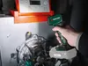 A hand holding a cordless LED work light, pointing it towards a piece of machinery. Produktbild-Vorschau