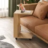 A wooden side table with wheels is placed next to a brown leather sofa in a living room. Produktbild-Vorschau