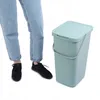 A person's legs and feet are shown next to a green trash can. Náhled obrázku produktu