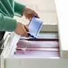 A person is placing a blue springform pan into a drawer filled with other baking items. Produktbild-Vorschau