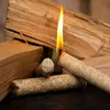 A close-up shot of several fire starters made of compressed wood wool, with one actively burning, set against a backdrop of larger pieces of wood. Produktbild-Vorschau