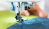 A close-up shot of a sewing machine needle stitching two pieces of fabric together. Produktbild-Vorschau