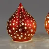 Two red decorative teardrop-shaped lamps with star cutouts, lit from within, are shown against a plain gray background. Produktbild-Vorschau