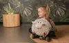 A young girl is sitting on the floor holding a plush sheep pillow. Produktbild-Vorschau