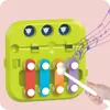 A child's hand is playing a toy xylophone with a mallet, with musical notes depicted in purple emanating from the toy. Produktbild-Vorschau