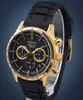 A close-up studio shot of a gold and black Seiko chronograph watch with a black rubber strap, displayed on a clear stand against a blue background. Náhled obrázku produktu
