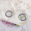 A close-up view of two grommets on a white curtain with a gold floral pattern. A pink hydrangea flower is visible beneath the curtain. Produktbild-Vorschau