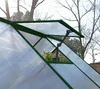 Close-up of a greenhouse roof vent opening, showing the automatic opener mechanism and some plants inside. Podgląd zdjęcia produktu
