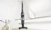 A black stick vacuum cleaner is displayed on a wooden surface in front of a staircase. Produktbild-Vorschau