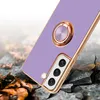 A purple phone case with a gold ring holder is shown on a cracked, rocky surface with fallen leaves. Produktbild-Vorschau