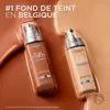Two bottles of L'Oréal True Match foundation are displayed on a glossy, liquid-like background in shades of brown and beige. Voir les images du produit