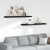 Two black floating shelves mounted on a white wall above a grey sofa, decorated with various items. Náhled obrázku produktu