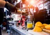 A person wearing black gloves is using a manual citrus juicer to extract juice from oranges. A jar of orange juice and cut oranges are visible on the counter. Podgląd zdjęcia produktu