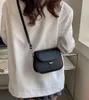 A woman wearing a white blazer and a grey skirt is carrying a black leather crossbody bag. Náhľad obrázku produktu