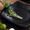 A black square plate with pea shoots on it, with a lime and part of an onion in the foreground. Náhled obrázku produktu