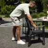 A man is arranging chairs around a table in a garden setting. Produktbild-Vorschau