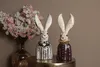 Two decorative rabbit figurines are displayed on a table next to a vase of flowers. Produktbild-Vorschau