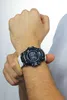 A person wearing a white t-shirt and a black and blue G-Shock watch on their left wrist. Produktbild-Vorschau