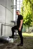 A man stands next to a large industrial silo, with his left foot on a metal pipe. Produktbild-Vorschau