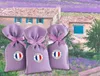 Three lavender sachets are displayed in front of a picturesque scene of a house in a lavender field. Produktbild-Vorschau