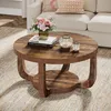 A round coffee table with a two-tiered design, featuring a rustic brown wood finish. It is placed on a textured rug in a living room setting, with a sofa and decorative items visible in the background. Anteprima dell’immagine prodotto