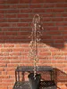 A potted weeping willow tree with catkins stands in front of a red brick wall, placed on a black metal stand. Produktbild-Vorschau