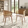 Two dining chairs with rattan backs and beige velvet seats are placed on a patterned rug in a well-lit room with a large window and a cabinet in the background. Voir les images du produit