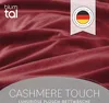 A close-up of dark red plush fabric, likely bedding, with brand logo and marketing text overlay. Voir les images du produit