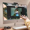 A person's hand is reaching towards an all-in-one computer displaying a video call. Produktbild-Vorschau