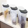 Three clear plastic food storage containers with black lids are lined up on a countertop. Produktbild-Vorschau