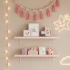 A decorated wall with two pink shelves holding decorative items, artwork, and books, with string lights on the left and neon signs on the right. Anteprima dell’immagine prodotto