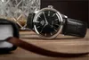 A watch is placed on a wooden surface next to a glass of whiskey and a leather-bound book. Produktbild-Vorschau