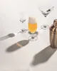 A collection of glassware and a cocktail shaker on a white surface, with dramatic shadows. Anteprima dell’immagine prodotto