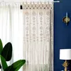 A macrame curtain hangs in front of a window, with a blue wall and a lamp in the background. Produktbild-Vorschau