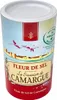 A cylindrical container of Fleur de Sel de Camargue salt, featuring a scenic illustration of flamingos flying over a coastal town. Voir les images du produit
