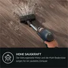 A hand holding a cordless vacuum cleaner on a wooden floor, with dust being picked up. Produktbild-Vorschau